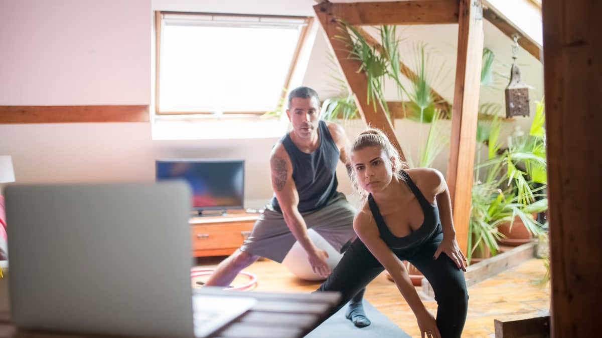 A man and woman working out at home using a laptop for guided exercises. Indoor active lifestyle.